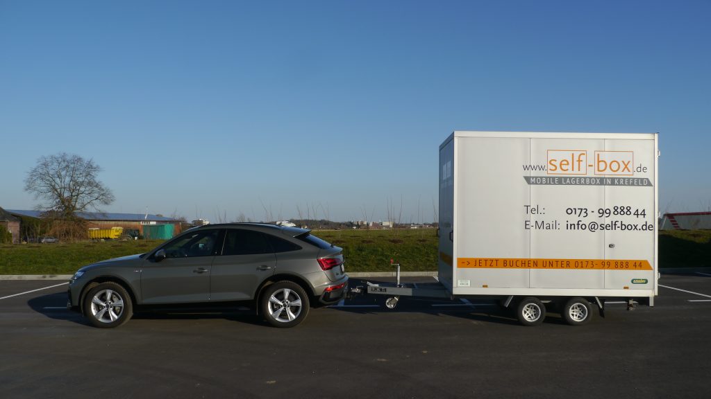 Selfbox-Anhänger angehangen an ein Auto auf einem Parkplatz stehend